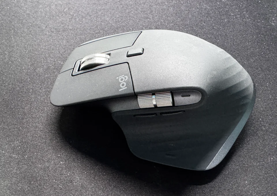 เมาส์ Logitech MX Master สีเทาเข้ม มองเห็นล้อเลื่อนโลหะแบบมีร่อง ปุ่มควบคุมด้านข้าง และโลโก้ logi ตัวเมาส์มีคราบฝุ่นและรอยการใช้งาน